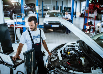 Mechaniker steht neben der offenen Motorhaube eines Autos